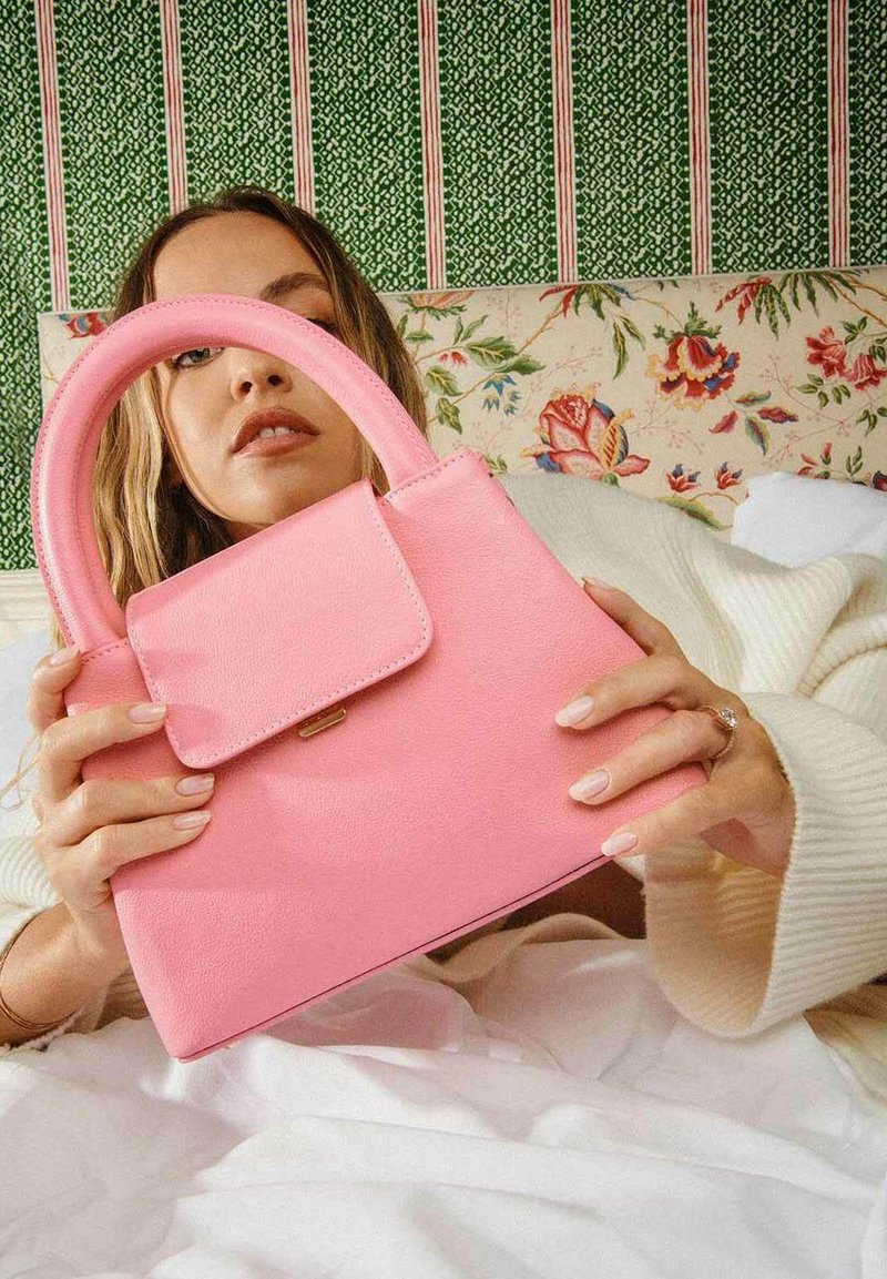 Sac à main en cuir rose au design structuré et muni d'une anse supérieure. Comprend une poche à rabat à l'avant et des détails de couture visibles.