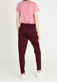 Burgundské tepláky s elastickým pasem, které jsou kombinovány se světle růžovým tričkem s krátkým rukávem a bílými teniskami.