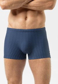 Marineblaue Boxershorts mit einem geometrischen Muster in Hellblau. Hergestellt aus dehnbarem Stoff, sitzen sie eng anliegend und haben einen elastischen Bund.