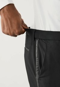 Schwarze, maßgeschneiderte Hosen aus strukturierter Stoff, mit geradem Schnitt, seitlichen Taschen und einem kontrastierenden grauen Streifen entlang der Nähte.