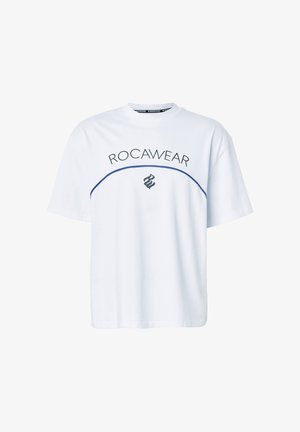 Bílé tričko s krátkými rukávy s nápisem "ROCAWEAR" a tmavě modrou zakřivenou čárou a plamenovým logem pod nápisem na přední straně.