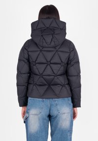 Giacca a vento nera con design a rombi, cappuccio attaccato, polsini elasticizzati e taglio corto, abbinata a jeans azzurri chiari.