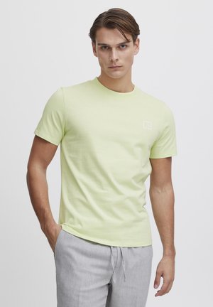 Helles grünes T-Shirt mit kurzen Ärmeln aus glattem Baumwollstoff, mit einem Rundhalsausschnitt und einem kleinen weißen Logo auf der linken Brust.