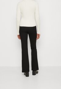 Czarne spódnice w stylu dzwonów o gładkiej teksturze i dopasowanej talii. W połączeniu z jasnym, prążkowanym topem z długim rękawem w kolorze kremowym.