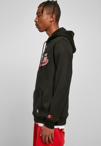 Sweat-shirt à capuche noir avec un graphique rouge sur le devant, poche kangourou, poignets côtelés et détail de logo sur la manche. Associé avec un short rouge.