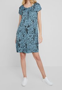 Krótka sukienka z rękawami do łokci, luźno dopasowana, w jasnoniebieskim kolorze z czarnym wzorem zwierzęcym. Miękka tkanina z okrągłym dekoltem i prostym dołem.