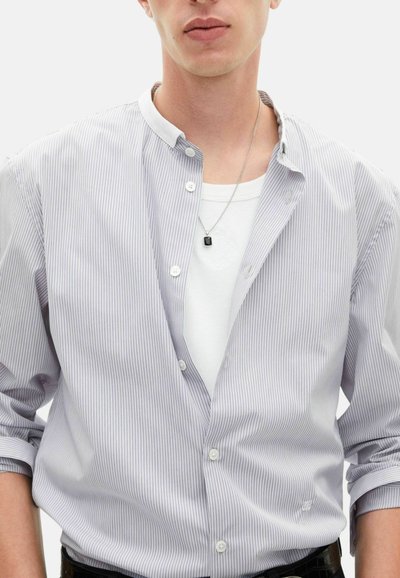 Wrzosowa koszula w paski w odcieniach jasnego niebieskiego i białego, z otwartym kołnierzem, noszona na białym t-shircie z okr�ągłym dekoltem, do której dodano srebrny naszyjnik.