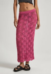 Gonna all'uncinetto rosa con un design lungo e fluttuante, caratterizzato da motivi a trama aperta. Abbinata a sandali neri.