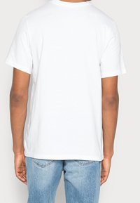 Vit bomulls-t-shirt med klassisk passform, rund halsringning och korta ärmar, i kombination med ljusblå denimjeans. Slät textur, utan mönster.