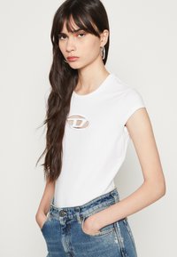 Witte T-shirt met korte mouwen en een ronde halslijn, voorzien van een uitgesneden logodetail op de borst. Gepaard met hoge taille blauwe jeans.