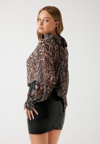 Blusa trasparente a maniche lunghe con stampa serpente, caratterizzata da un collo alto e una vestibilità ampia. Abbinata a una mini gonna in ecopelle nera.