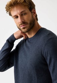Maglione lavorato a maglia blu navy con un motivo a diamante testurizzato, dotato di collo rotondo e maniche lunghe. Tessuto morbido con una silhouette aderente.