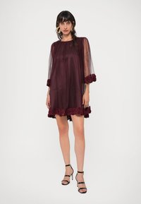 Βουργουνδί φόρεμα από τούλι με λουλουδάτα δαντελένια διακοσμητικά στα μανίκια και το στρίφωμα. Διαθέτει διάφανα μακριά μανίκια και άνετη γραμμή, που συνδυάζεται τέλεια με ψηλές γόβες.