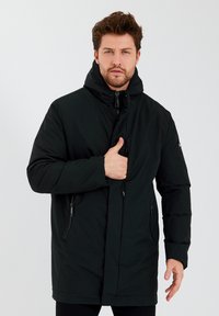 Zwarte donzenjas met capuchon, volledige ritssluiting aan de voorkant, zijzakken en een verstelbare sluiting. Soepele textuur en ontwerp tot aan de knieën.