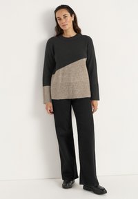 Lässiger Pullover in Dunkelgrau und Beige mit diagonaler Gestaltung, Rundhalsausschnitt und geripptem Saum. Kombiniert mit weiten schwarzen Hosen.