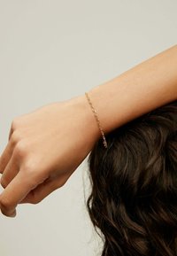 Pulsera de oro hecha de delicados eslabones de cadena, llevada en una muñeca. Presenta una textura suave con un brillo sutil contra la piel.