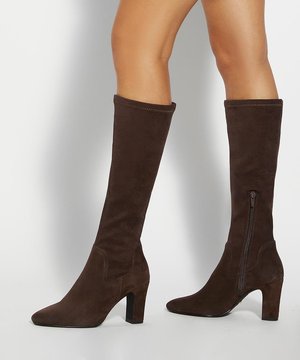 Bottes marron en daim montantes jusqu'au genou avec talons blocs et fermeture éclair latérale portées sur des jambes nues sur un fond uni.