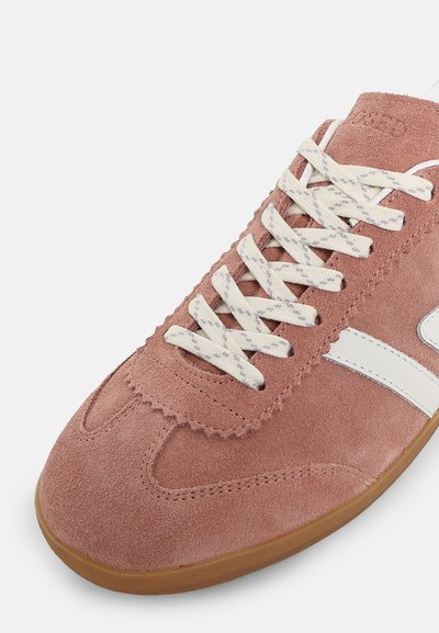 Gros plan sur une basket en daim rose avec des lacets blancs, une bande blanche latérale et une semelle en gomme naturelle sur fond blanc.