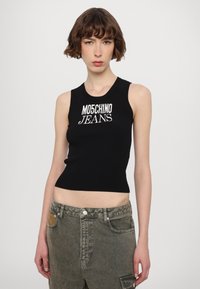 Melnā ribota bezpiedurkņu tvertne ar baltu "MOSCHINO JEANS" logo. Pieguļošs dizains, apaļa kakla izgriezums. Apvienota ar olīvu zaļajiem cargo biksēm.