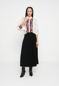 Bluza s više uzoraka s podvrnutim rukavima, ukrašena zlatnim lancima, tamnoplave i crvene pruge. Crna plisirana maksi suknja. Crne gležnjače.