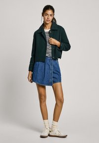 Tmavozelená skrátená bunda s golierom, pruhovaný čierno-biely top, modrá denimbová sukňa, biele topánky, béžové ponožky. Jednoduchý dizajn a voľný strih.