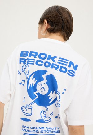 White oversized t-shirt featuring a blue graphic design of a cartoon character with a broken record, text reading "Broken Records," and musical notes.