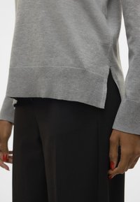 Šedý svetr s žebrovanými manžetami a spodním lemem, s postranními rozparky. V kombinaci s černými ušitými kalhotami. Jemná pletená textura.