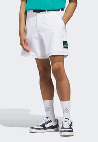 Bílé šortky s černým a tyrkysovým logem Adidas. Mají volný střih, boční kapsy a prošité lemy. Nosí se s bílými ponožkami a teniskami.