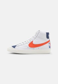 Tenisky s vysokým střihem, bílý kožený svršek, oranžový znak Nike, námořnické akcenty, gumová podrážka a záplata loga NBA na patě.