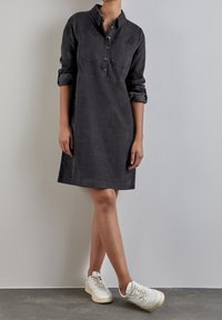 Vestito button-up grigio carbone con colletto, due tasche sul petto, maniche arrotolate e sneaker bianche. Tessuto morbido, taglio dritto, lunghezza a metà coscia.