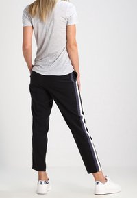 Grey cotton t-shirt paired with black tapered pants featuring vertical stripes in navy and white, with white sneakers that have silver accents.