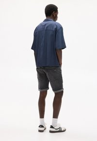 Cămașă bleu cu mânecă scurtă, cu o croială lejeră, asortată cu șorturi din denim închise la culoare și tenisi albi. Textură netedă, șorturi răsucite și un design minimal.