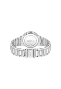 Reloj de plata con pulsera de acero inoxidable y caja redonda. Presenta un acabado liso y pulido, y un logotipo grabado en la parte posterior.