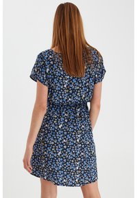 Květinové šaty z tmavě modré látky s krátkými rukávy, zúženým pasem a vícebarevným vzorem malých květin pokrývající celou plochu.