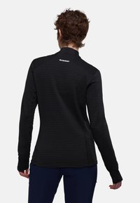 Langärmliges schwarzes Oberteil mit einem strukturierten, gestreiften Muster, hohem Kragen und Daumenlöchern in den Bündchen. "Mammut"-Logo auf dem Rücken angebracht.