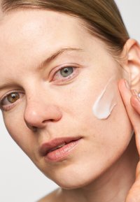 Crema idratante bianca applicata su un volto con carnagione chiara, visibile texture, sopracciglia naturali e un colore labbra sottile.