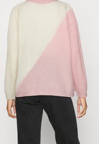 Pull en maille présentant un design en blocs de couleurs pastel avec du blanc et du rose clair. Manches longues et encolure côtelée. Tissu texturé, coupe ample.