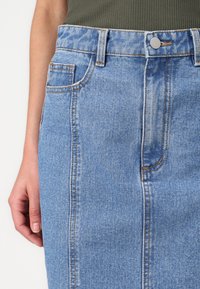 Sinine denim seelik sirge lõikega, millel on nööpkinne, ees taskud ja kontrastne õmblus äärtes.