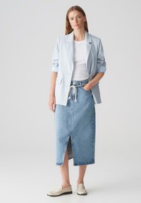 Blazer azzurro chiaro sopra una maglietta bianca; abbinato a una gonna di jeans a vita alta con uno spacco frontale. Mocassini beige completano il look.