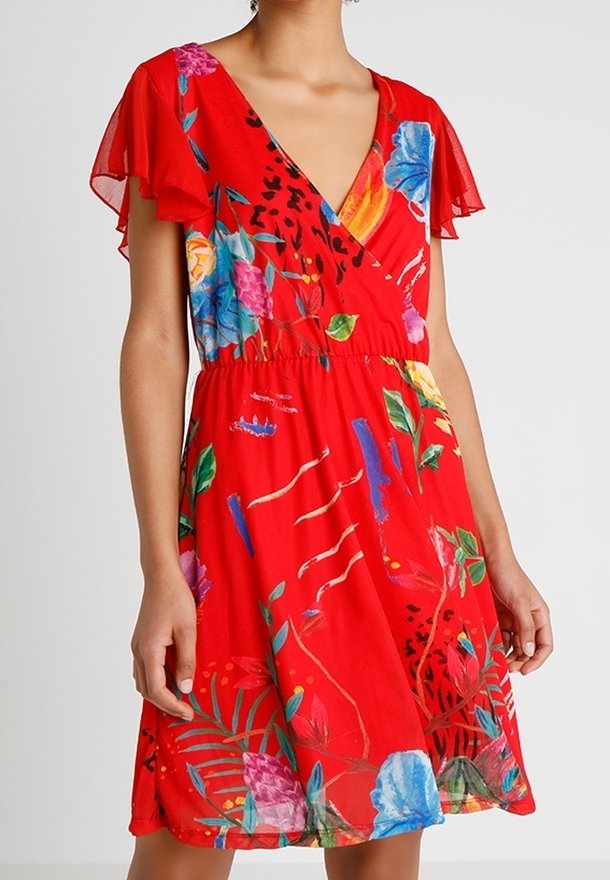 Femme portant une robe portefeuille rouge à fleurs avec des manches volantées et une taille froncée, présentant des motifs floraux colorés bleu, rose et vert.