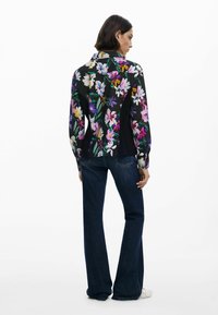 Camicia floreale con sfondo nero, caratterizzata da fiori multicolori vivaci, design con colletto e maniche lunghe abbinate a jeans in denim scuri.