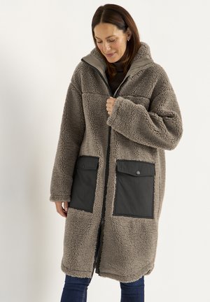Vollig beige fuzzy jas met een ritssluiting aan de voorkant, grote grijze patchzakken en een capuchon. Bevat een zachte, gestructureerde stof en een losse pasvorm.