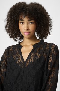 Schwarze Spitze Bluse mit floralen Mustern, tiefem V-Ausschnitt und Rüschensaum. Der Stoff ist semi-transparent und hat lange Ärmel.