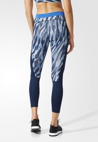 Leggings aus dehnbarem Stoff, mit einem blau-weißen abstrakten Muster, mittelhoher Taille und verkürzter Länge. Es werden schwarze Sportschuhe getragen.