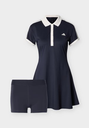 Kratka polo haljina mornarsko plave boje s bijelim ovratnikom i manžetama, uparena s pripijenim mornarsko plavim šortsevima, s malim bijelim logom na prsima.