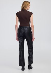 Top aderente marrone con maniche corte, abbinato a pantaloni in pelle nera a vita alta con tasche e design a gamba dritta.