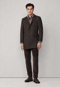 Abrigo marrón a cuadros con solapa de muesca, dos botones y bolsillos de parche, combinado con pantalones oscuros y zapatos de cordones. Adecuado para el clima fresco.