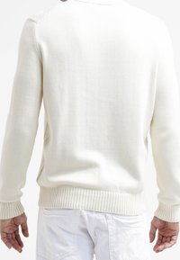 Ljus krämfärgad stickad tröja med ribbade muddar och fåll, med en texturerad finish. Designen är enkel, med rundad hals och avslappnad passform.