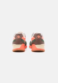 Une paire de baskets marron, verte et corail avec un revêtement intérieur blanc, vue de l'arrière, affichant un logo sur la zone du talon.