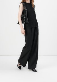 Czarna koronkowa bluzka z falbanastym dekoltem, zestawiona z czarnymi spodniami w szerokim kroju i błyszczącymi szpilkami. Czarna torebka o strukturalnym fasonie.